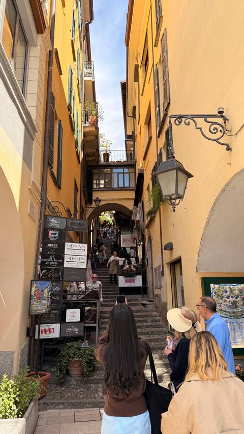 Charming narrow alley with stairs, shop signs and yellow walls bustling with visitors.