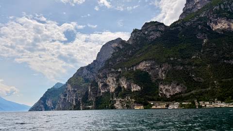 Steep limestone cliffs plunging into deep blue lake waters under scattered clouds.