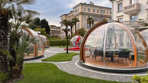 Modern hotel garden with transparent dome dining pods, manicured lawns and palm trees.