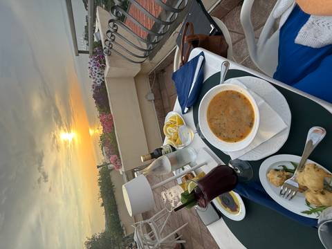 Outdoor dinner table set with soup, drinks and sea view at sunset on the Amalfi Coast