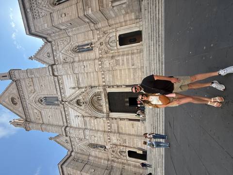 Smiling couple poses in front of the ornate façade of Naples Cathedral on a sunny day