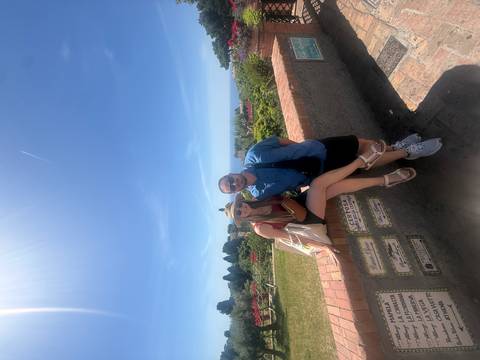 Couple poses against a brick wall overlooking colorful gardens and distant sea