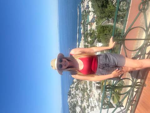 Woman in sunhat smiles with elevated view of Capri town and bright blue sea behind