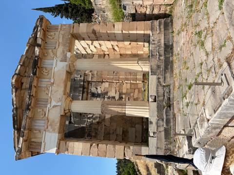 Weathered stone Athenian Treasury with Doric columns set against bright blue sky in Delphi