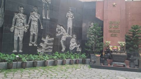 Outdoor memorial wall featuring sculpted reliefs of prisoners with an altar of incense and offerings in front.