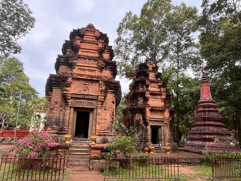Ancient brick temple towers surrounded by flowering shrubs and tall trees under a bright sky.