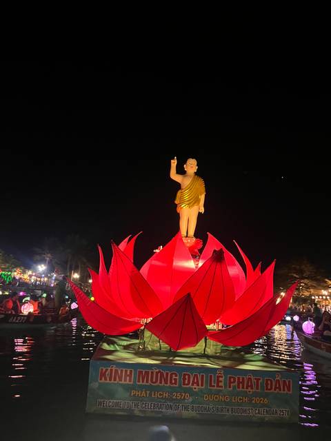 Large illuminated lotus float with a small Buddha statue pointing upward during a night festival.
