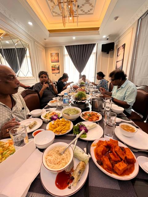 Group of travellers sharing a Vietnamese meal at a restaurant table covered with diverse dishes and drinks.