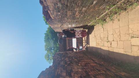 Woman standing between ancient brick walls on a sunlit stone path at an archaeological site.