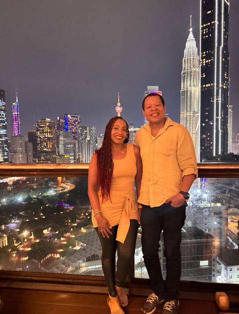 Evening rooftop shot of a couple with Kuala Lumpur’s illuminated skyline, including the Petronas Towers and KL Tower, behind them.