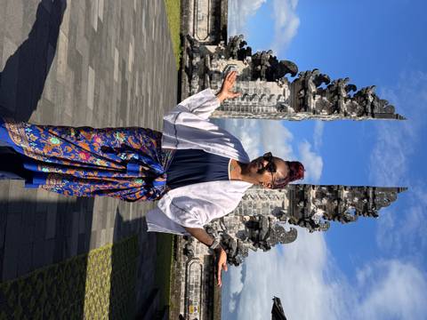 Woman dressed in sarong poses between intricately carved split gates against a blue sky at Bali’s Lempuyang Temple.