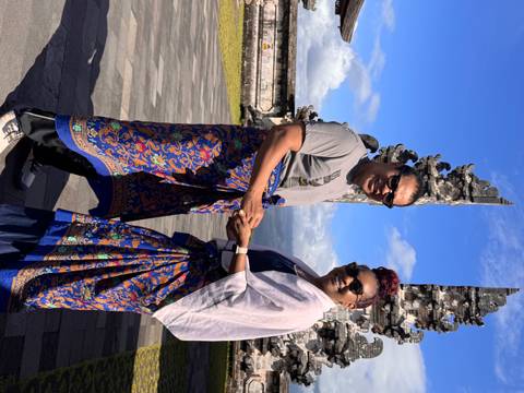 Couple dressed in sarongs hold hands near ornate stone pillars of Bali’s temple complex.