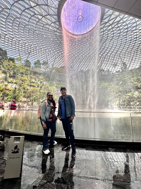 Travellers stand in front of the misty indoor waterfall under the glass dome of Jewel Changi Airport.