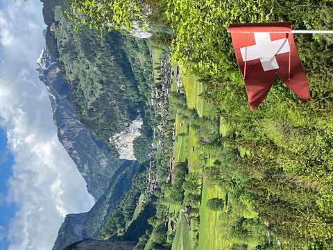 Verdant Swiss valley dotted with farms and framed by high alpine cliffs, Swiss flag in foreground