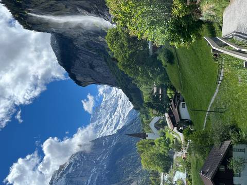 Picturesque alpine village with steepled church beneath snow-clad mountain cliffs and blue sky