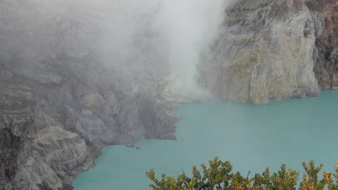 Turquoise acidic crater lake emits thick white sulphur steam from rugged volcanic walls