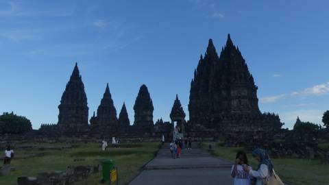 Silhouetted Hindu temple towers stand against a clear evening sky as visitors explore the site