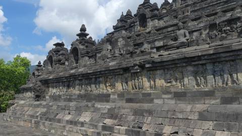 Side view of Borobudur’s stone terraces with carved reliefs and Buddha statues under clouds