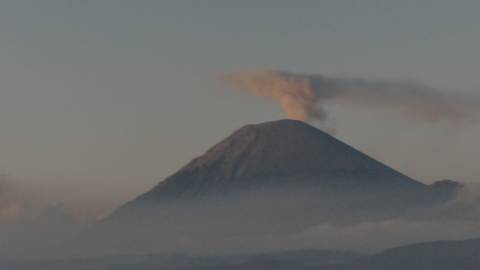 Distant volcano emits plume of smoke above low clouds at dawn