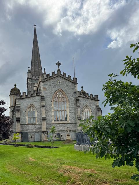 Stone-walled church with pointed spire framed by leafy trees