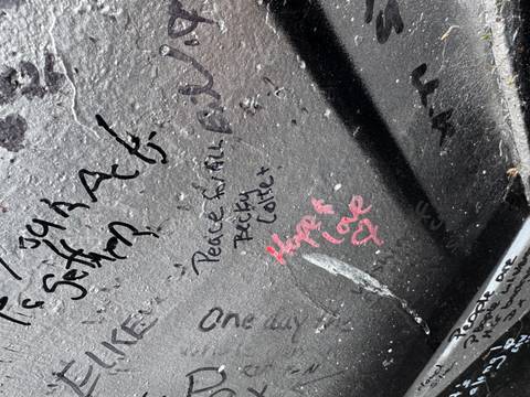 Close-up of graffiti messages and signatures on a dark mural wall