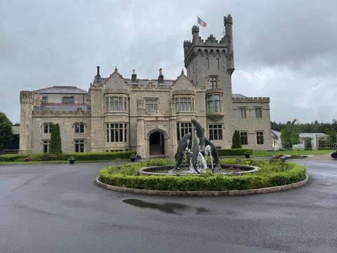 Grand manor-style castle hotel with fountain and dolphin statues on a grey, rainy Irish day.