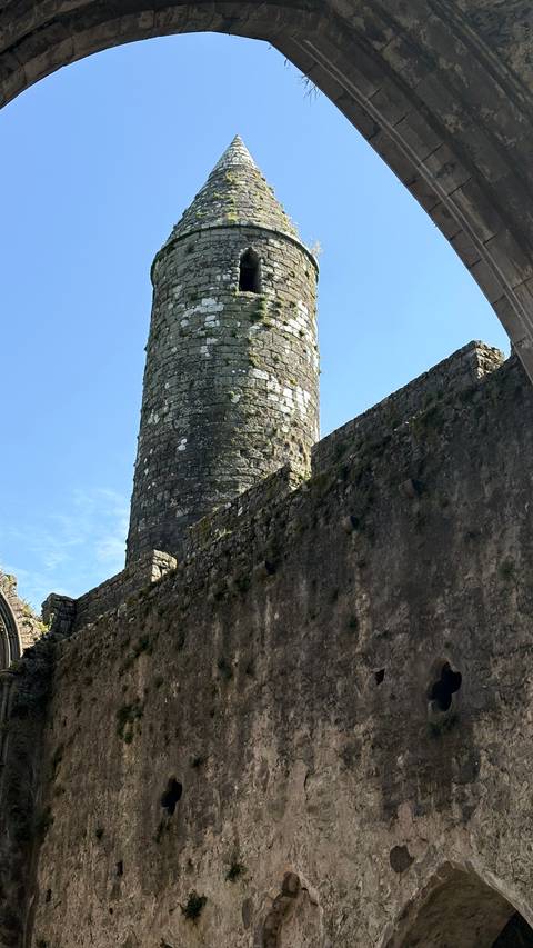Ancient round stone tower rising above thick castle walls under blue sky