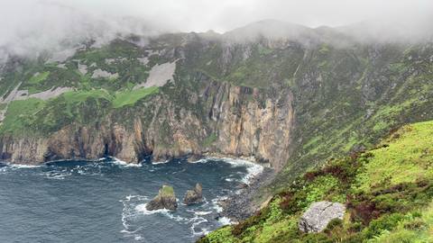 Misty high sea cliffs with crashing waves and green slopes at Slieve League