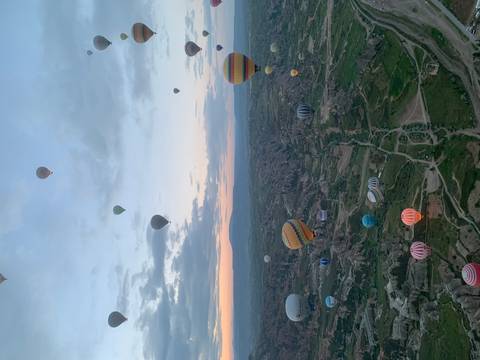 Dozens of hot-air balloons drift above the surreal valleys of Cappadocia at dawn.