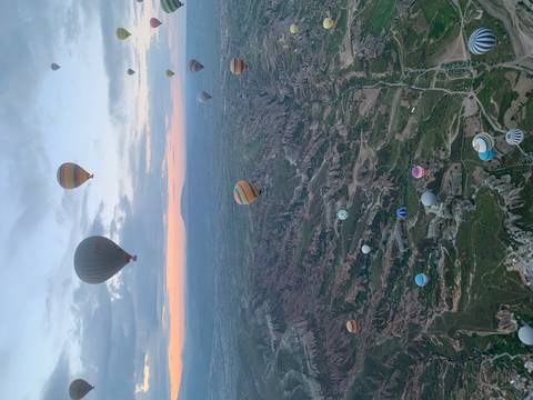 Wide aerial view of Cappadocia’s dramatic landscape dotted with dozens of hot-air balloons.