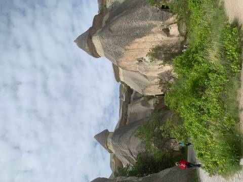 Travellers walk beneath towering fairy-chimney rock formations under a partly cloudy sky.