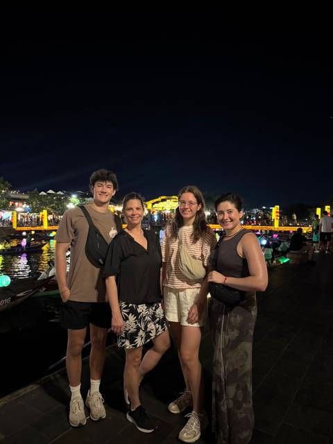 Four travelers posing at night beside a lantern-lit river bridge in Hoi An old town.