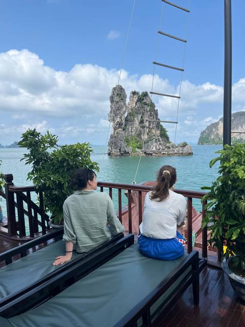 Two women relaxing on a boat deck overlooking turquoise waters and limestone karst islets of Halong Bay.