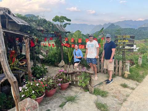 Travelers posing outside a rustic cafe decorated with Vietnamese flags amid lush mountain scenery.