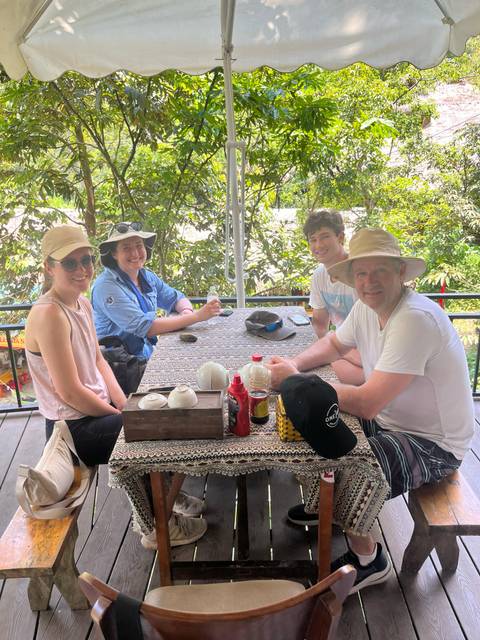 Small group sitting at an outdoor table under leafy trees enjoying drinks during the day.
