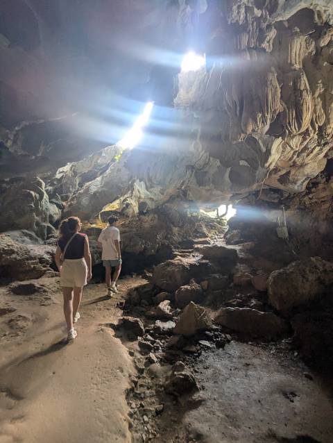 Travelers exploring the interior of a limestone cave with sunlight streaming through an opening.