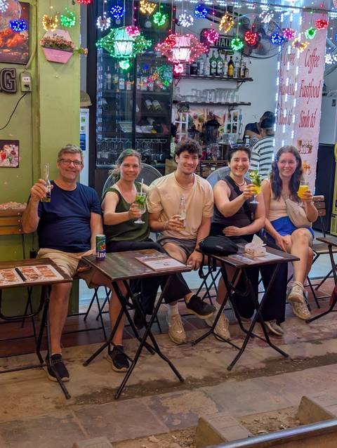 Group of five people sitting at small tables on a Vietnamese street enjoying colorful drinks and beer.