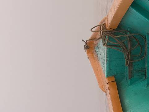 View from the bow of a small wooden boat pointing into dense white fog on a calm river, with a coiled rope resting on the deck.