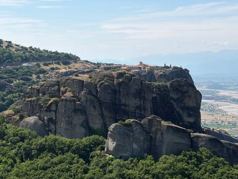 Dramatic rock pillars crowned by an ancient monastery overlook a lush valley in Meteora, Greece.