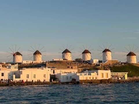 Iconic white windmills of Mykonos line the hilltop, glowing in golden evening light above the sea.