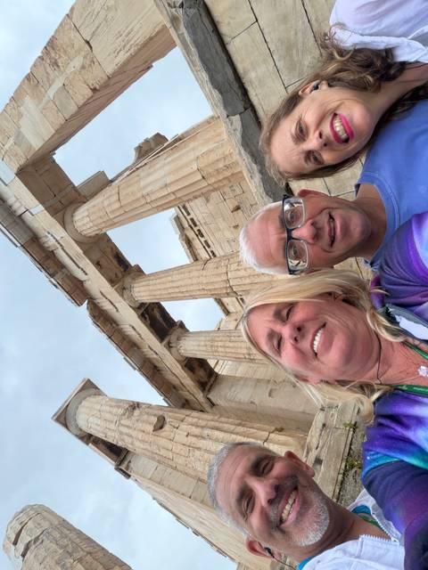 Selfie of travellers beneath towering marble columns of the Acropolis in Athens.