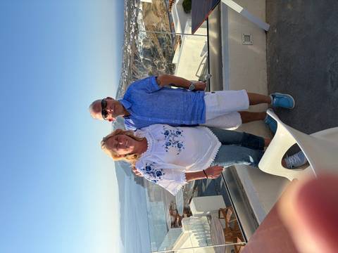 Couple stands on a balcony overlooking Santorini’s caldera and whitewashed villages.