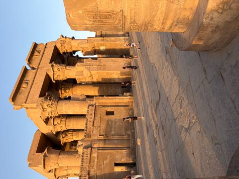 Tourists explore the impressive sandstone columns and carvings of an ancient Egyptian temple in warm afternoon light.