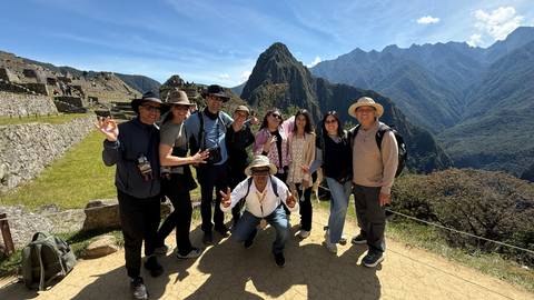 Tour group celebrating at the iconic Machu Picchu terraces with Huayna Picchu peak behind.