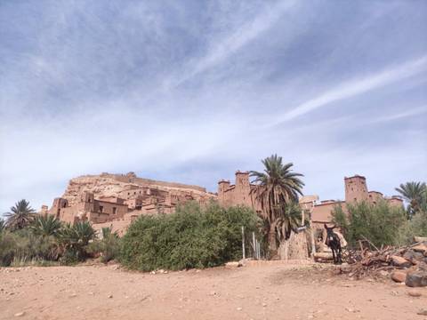 Mud-brick kasbah structures rise above palms beneath a lightly clouded sky in southern Morocco.