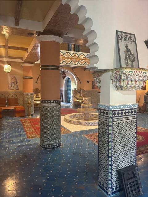 Opulent Moroccan riad interior featuring mosaic tiles, arches, carpets and a central fountain.