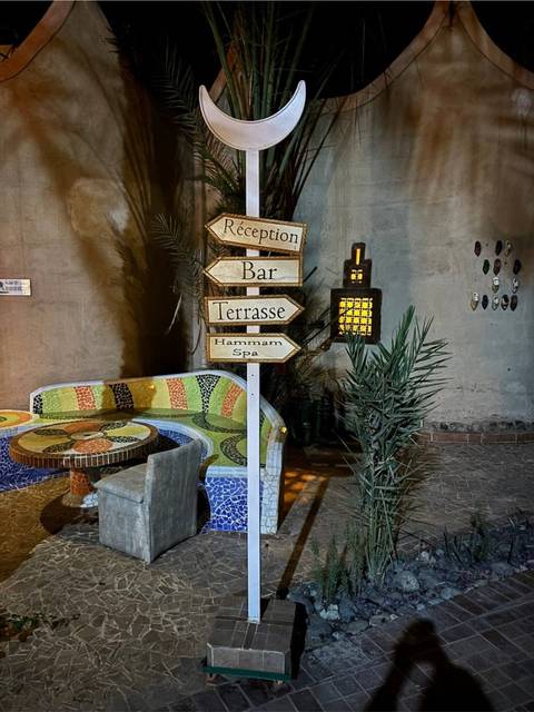 Rustic night-time courtyard with mosaic bench and wooden signposts pointing to reception, bar and spa.