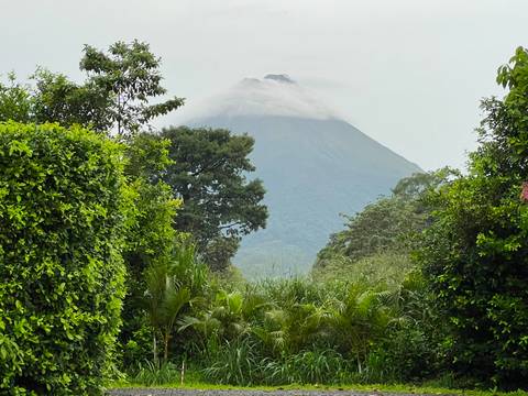 Dramatic view of cloud-shrouded Arenal Volcano framed by dense tropical greenery.