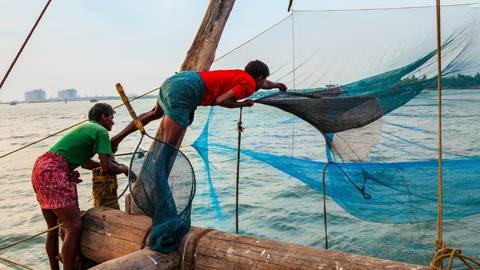 Local fishermen working on large Chinese fishing nets over coastal waters.