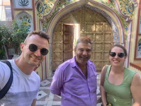 Three travelers smiling for a selfie in front of an ornately carved wooden doorway with colorful arch details.